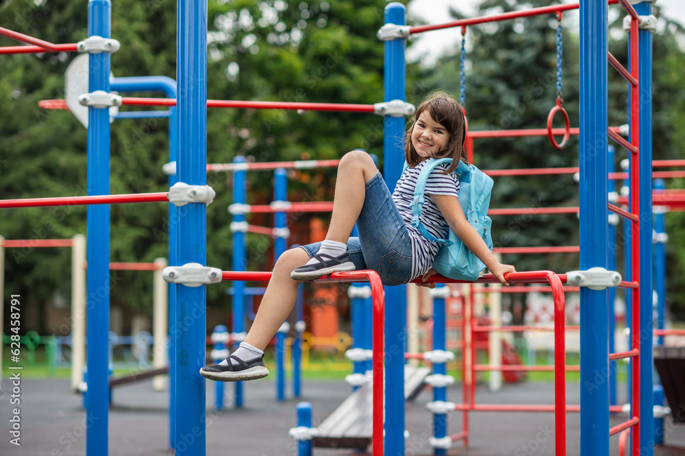 Fototapeta premium back to school. happy smiling child girl 11 years old teenager with a backpack.stands on the background of the sports ground near the school. High quality photo