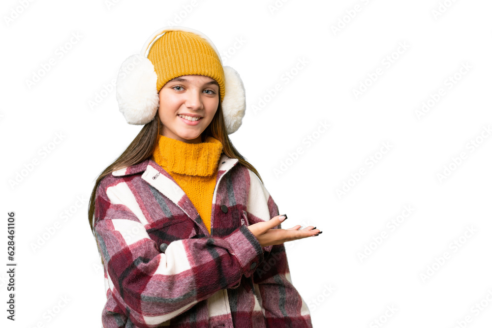 Teenager caucasian girl wearing winter muffs over isolated background presenting an idea while looking smiling towards Teenager caucasian girl wearing winter muffs over isolated background presenting an idea while looking smiling towards