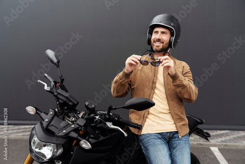 Photography Stylish smiling confident man, biker wearing helmet standing near sport motorcycle
