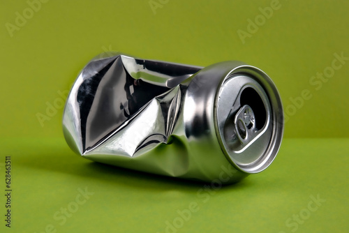 Aluminum crushed can for beverage. Still-life picture of a single metallic container isolated on green background.