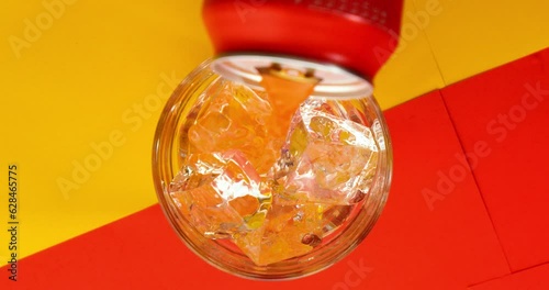 Birdeye slow motion shot of a filled glass with clear ice cubes whilte juice poured in glass on yellow red background photo