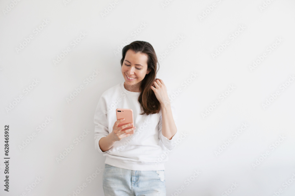 Young woman talking on mobile phone, smiling, using social media. Millennial person in white sweatshirt on white background. People using technology. Work call. Young woman talking on mobile phone, smiling, using social media. Millennial person in white sweatshirt on white background. People using technology. Work call.
