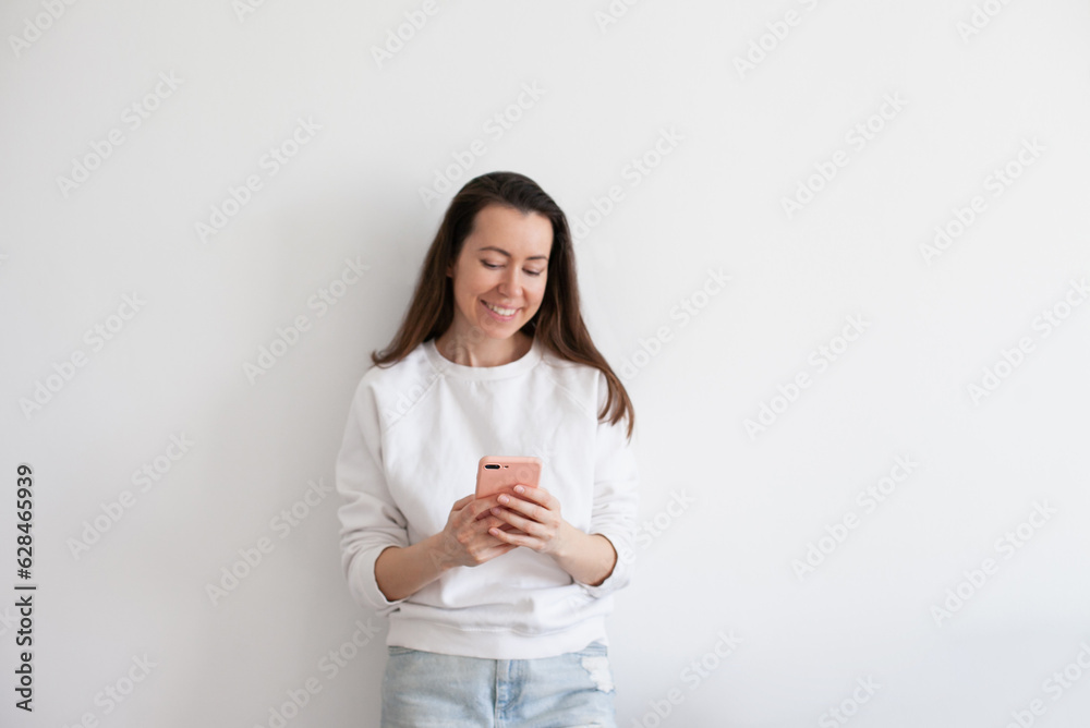 Young woman talking on mobile phone, smiling, using social media. Millennial person in white sweatshirt on white background. People using technology. Work call. Young woman talking on mobile phone, smiling, using social media. Millennial person in white sweatshirt on white background. People using technology. Work call.