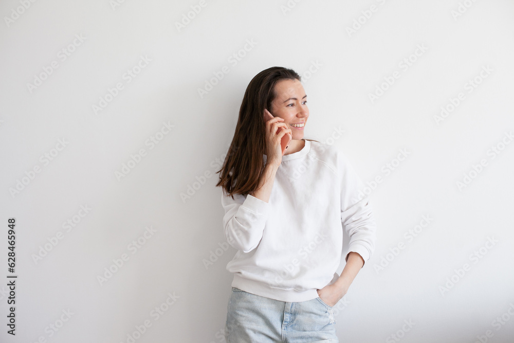 Young woman talking on mobile phone, smiling, using social media. Millennial person in white sweatshirt on white background. People using technology. Work call. Young woman talking on mobile phone, smiling, using social media. Millennial person in white sweatshirt on white background. People using technology. Work call.