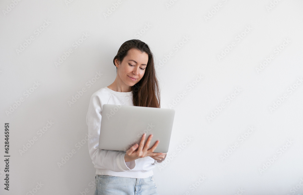 Young millennial woman wearing black hat using laptop, working online, white background. Copy space left and right. Young millennial woman wearing black hat using laptop, working online, white background. Copy space left and right.