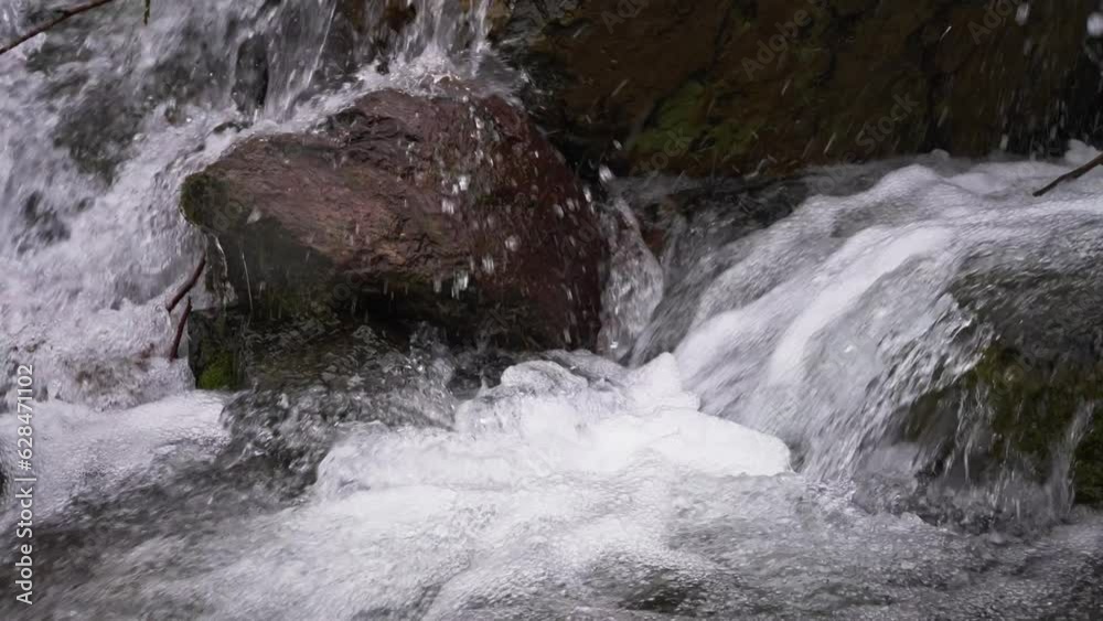 A stormy stream of a mountain stream flows through the stones. Pure water in a mountain stream is formed due to the melting of snow. A stormy stream of a mountain stream flows through the stones. Pure water in a mountain stream is formed due to the melting of snow.