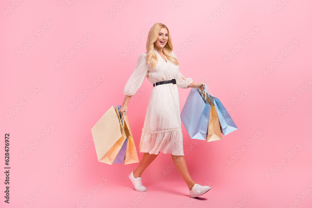 Full length body photo of walking attractive model young girl holding packages bargains fashionista chic isolated on pink color background