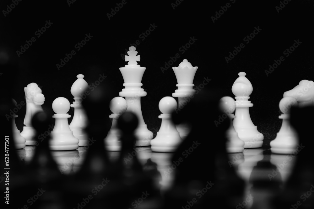 Focus on white chess pieces on the background. King and Queen with black chess pieces unfocused in front