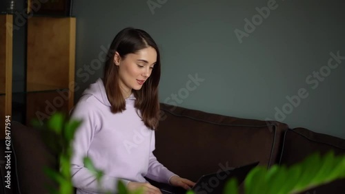 A girl sits on the couch, she works, studies online with a laptop. Girl typing on the keyboard and chatting with collegs