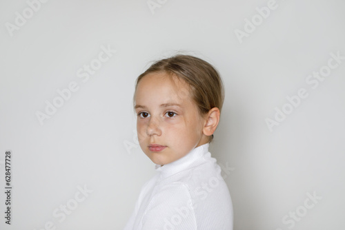 Cute serious child portrait. Young girl posing against white studio wall background