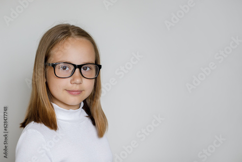 Portrait of smart young girl in glasses on white studio wall background