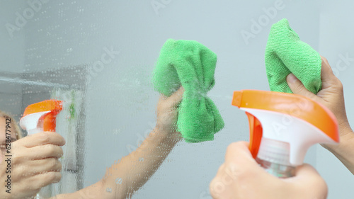 Cleaning and polish mirror with rag and spray in bathroom at home. Cropped shot of a young woman cleaning the mirror surface with sanitising spray and wipe.