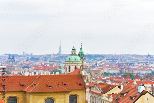 View of the old houses with a red tiled roof, church spire and dome, and cityscape. Ancient buildings. Prague, Czech Republic, October 2022.