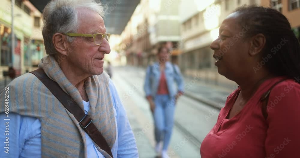 Multiracial senior people talking together while waiting at tram station in the city Multiracial senior people talking together while waiting at tram station in the city