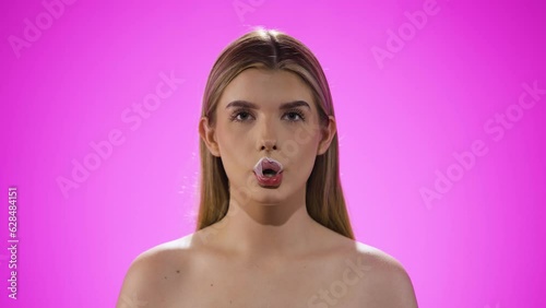 Joyful funny caucasian woman blows gum bubble in slow motion, happy face, studio photo