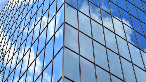 Structural glass wall reflecting blue sky. Abstract modern architecture fragment. Glass building with transparent facade of the building and blue sky. Contemporary architectural background.