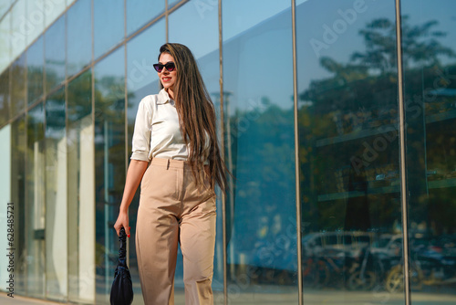 Stylish female model wearing sunglasses walking on city street.