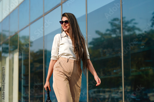Stylish female model wearing sunglasses walking on city street.