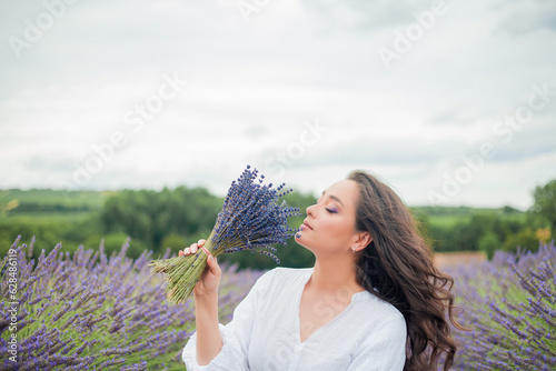 Lavender field. Beautiful dark-haired curly woman in white simple dress in field of purple flowers. Summer.