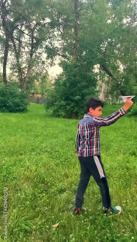 boy walks in a circle with a paper airplane in outdoors. Vertical video.