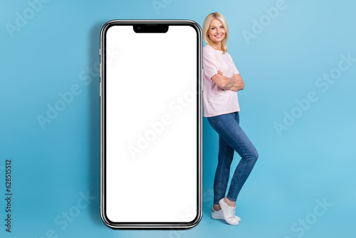 Full size photo of cheerful woman white t-shirt jeans sneakers lean on electronic touchscreen smartphone isolated on blue color background