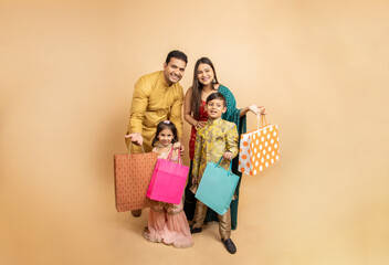Portrait of Happy indian family wearing traditional cloths holding shopping bags and celebration diwali festival together isolated on beige studio background. Parents with kids celebrate festive sale