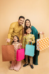 Happy young indian family wearing traditional cloths holding shopping bags and celebration diwali festival together isolated on beige studio background. Parents with kids celebrate festive season sale