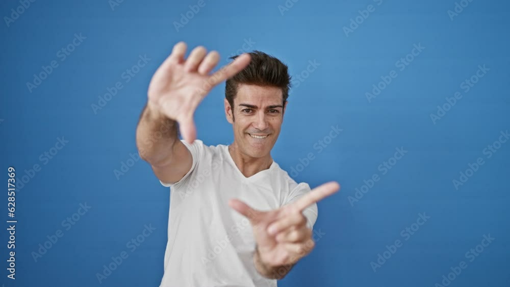 Young hispanic man doing photo gesture with hands smiling over isolated blue background Young hispanic man doing photo gesture with hands smiling over isolated blue background