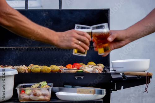men hold beer in their hands on the background of the grill, vegetables and meat. Selective focus.