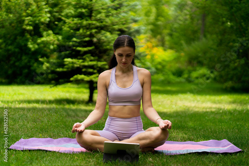 young girl on a grass field doing an online yoga class on a mat