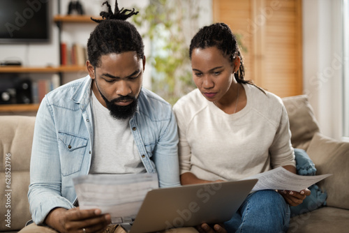 African American couple going through their financial bills while paying them over computer at home photo