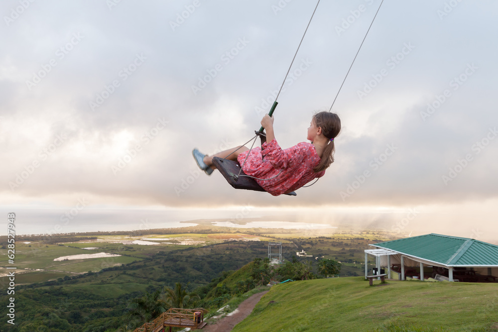 Little girl is on a swing under cloudy sky. Montana Redonda