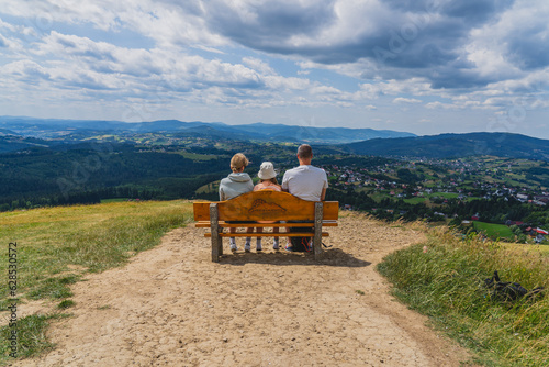 Fototapeta Naklejka Na Ścianę i Meble -  A family sitting on a bench located in the Beskids on the 