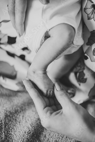 Baby feet in mom hands. Mother holding child s legs. Cute little infant lying on bed at home. Mom hold son legs. Closeup. Tiny  bare feet of newborn baby girl or boy. Sleep daughter. Black white photo
