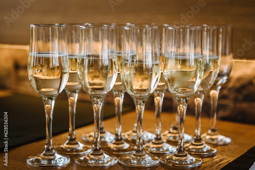 Glasses of champagne on table bar. Many glass of white wine. Buffet. Celebration of birthday, baptism, wedding or corporate party. Catering service. Serves glasses of sparkling wine. Closeup.