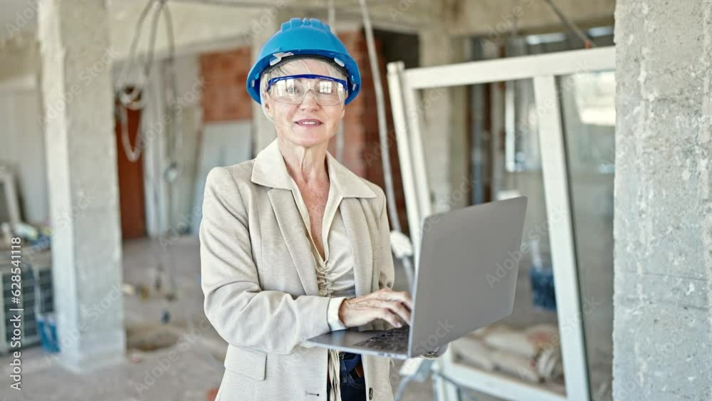 Middle age blonde woman architect smiling confident using laptop at construction site