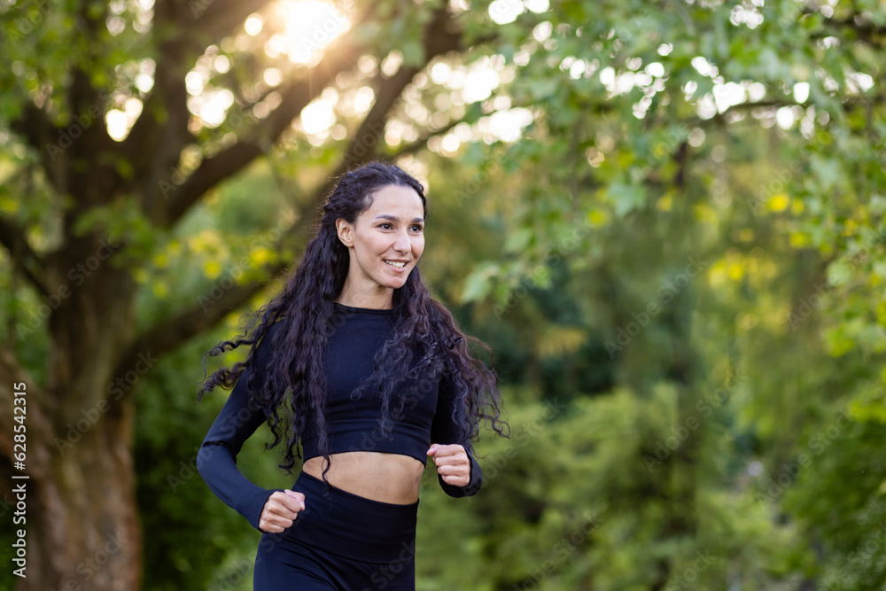 Young motivated and joyful woman jogging in the morning in a public park among trees, Hispanic woman with curly hair, slim in a tracksuit. Young motivated and joyful woman jogging in the morning in a public park among trees, Hispanic woman with curly hair, slim in a tracksuit.