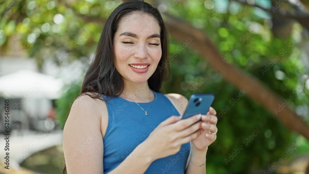 Young beautiful hispanic woman using smartphone smiling at park Young beautiful hispanic woman using smartphone smiling at park