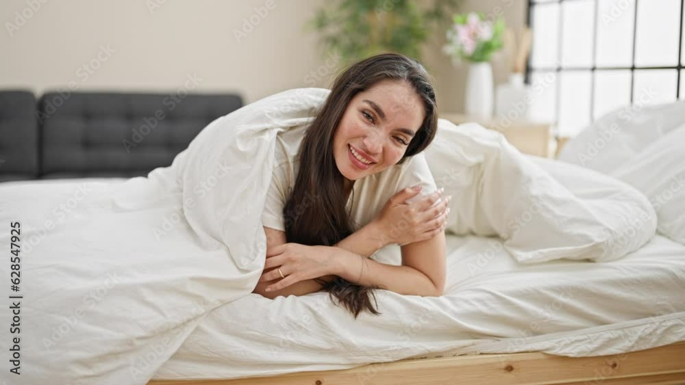 Young beautiful hispanic woman lying on bed covering with bedsheet at bedroom Young beautiful hispanic woman lying on bed covering with bedsheet at bedroom
