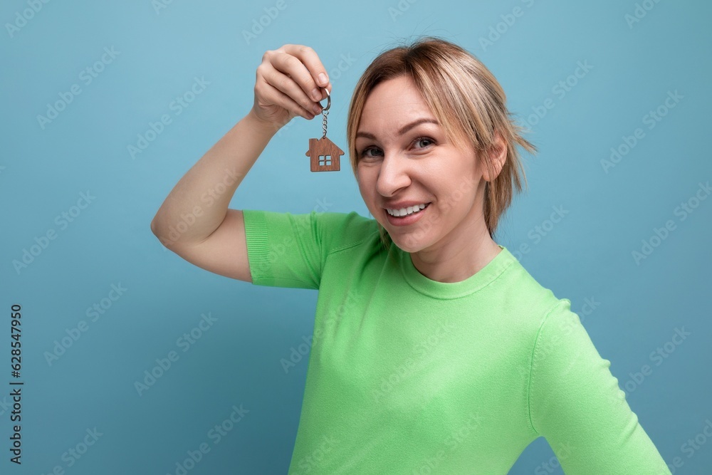 Fototapeta premium close-up of an attractive joyful blond girl in a casual outfit who shows off her infestation in the form of a home purchase on a blue background