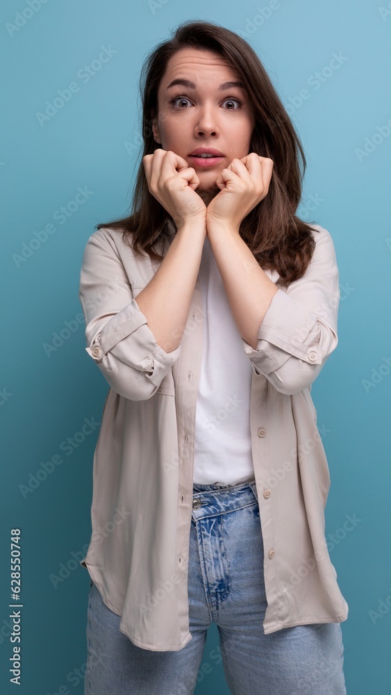 surprised brunette 30 year old female person dressed in a shirt and jeans looks at the camera on a blue background surprised brunette 30 year old female person dressed in a shirt and jeans looks at the camera on a blue background
