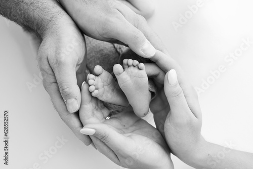 Fotografia The palms of the father, the mother are holding the foot of the newborn baby on white background