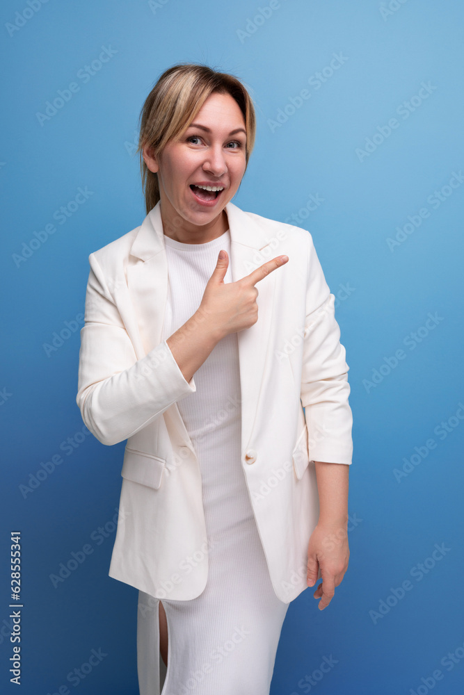 well-groomed young caucasian blond lady in a white jacket and dress points her finger to the sides well-groomed young caucasian blond lady in a white jacket and dress points her finger to the sides