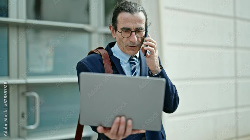 Middle age man business worker using laptop talking on smartphone at hospital