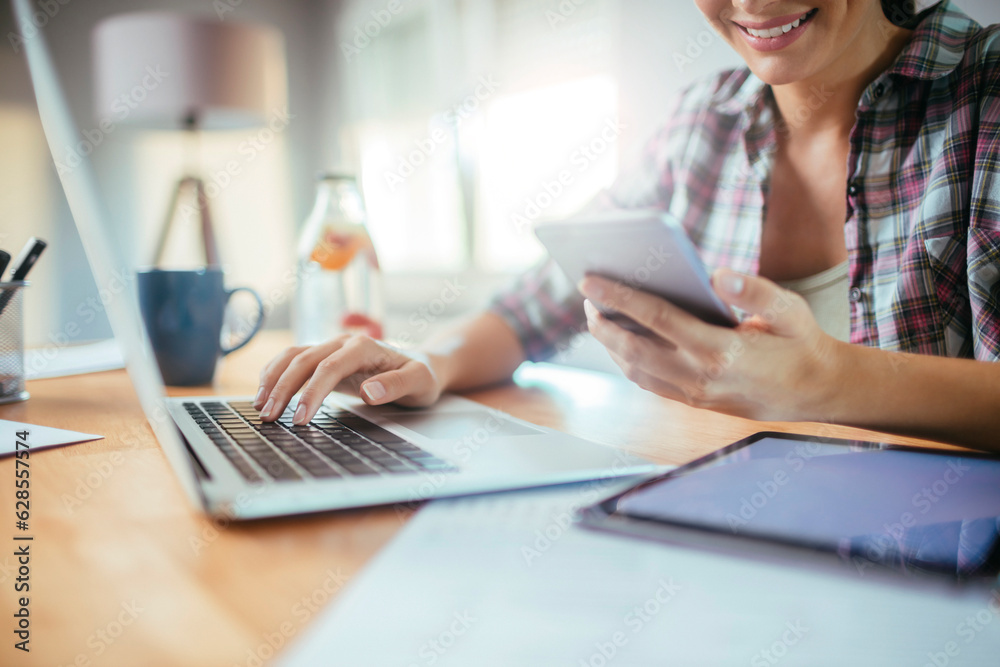 Young woman using a smart phone and laptop at home while working and studying