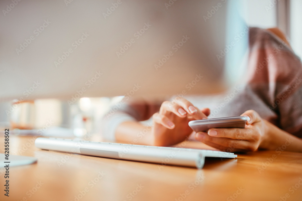 Fototapeta premium Young woman using a smart phone at home while working on her computer