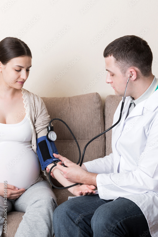 Young doctor is checking blood pressure of pregnant woman at home. High pressure problem during pregnancy concept Young doctor is checking blood pressure of pregnant woman at home. High pressure problem during pregnancy concept