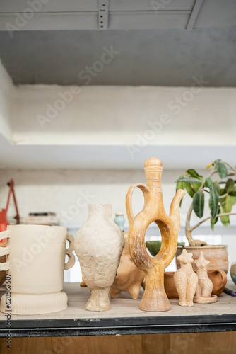 Different clay sculptures on rack near green plant in ceramic workshop