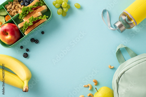 A nourishing school break scene from above, displaying a lunchbox with sandwiches accompanied by fruits, berries, water bottle and rucksack on blue isolated backdrop, perfect for text or advertising