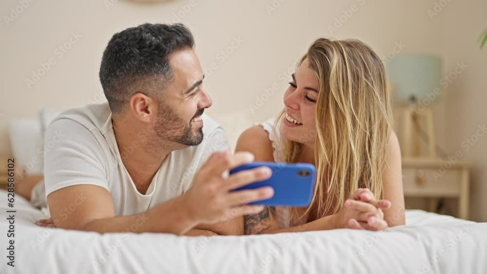Man and woman couple lying on bed using smartphone speaking at bedroom Man and woman couple lying on bed using smartphone speaking at bedroom
